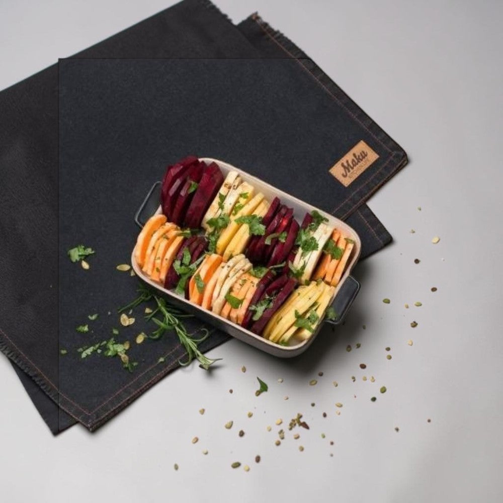 aelgmark black baking dish with layered root vegetables, including beets, sweet potatoes, and parsnips, garnished with herbs.