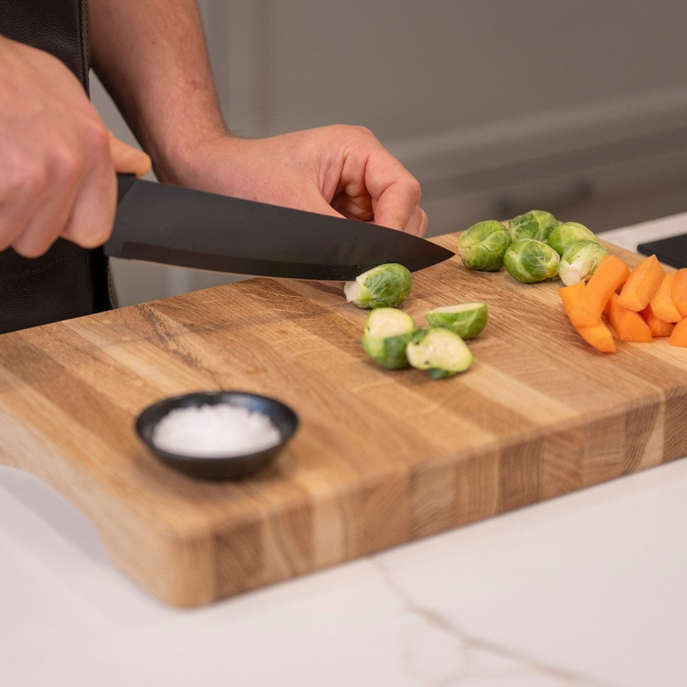 aelgmark black stainless steel 5-piece knife set for cooking, featuring a chef's knife slicing vegetables on a wooden cutting board.
