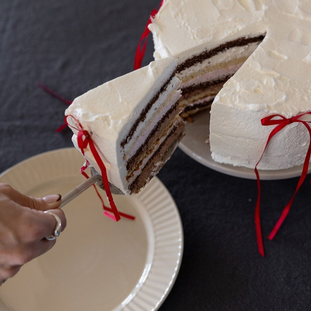 aelgmark Estelle stainless steel cake server with ribbed handle, serving a slice of layered cake with red ribbon accents.