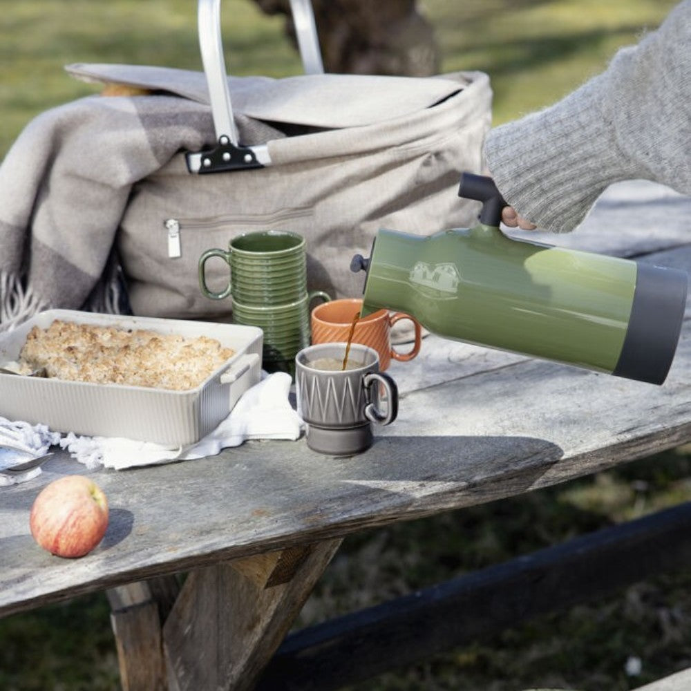 aelgmark Accent olive green stainless steel thermos pouring coffee into a mug during a picnic.