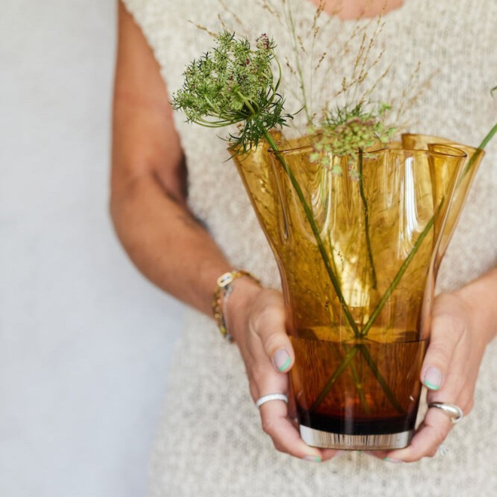 aelgmark Viva amber glass vase with ruffled edge, inspired by blooming flowers, holding delicate greenery.
