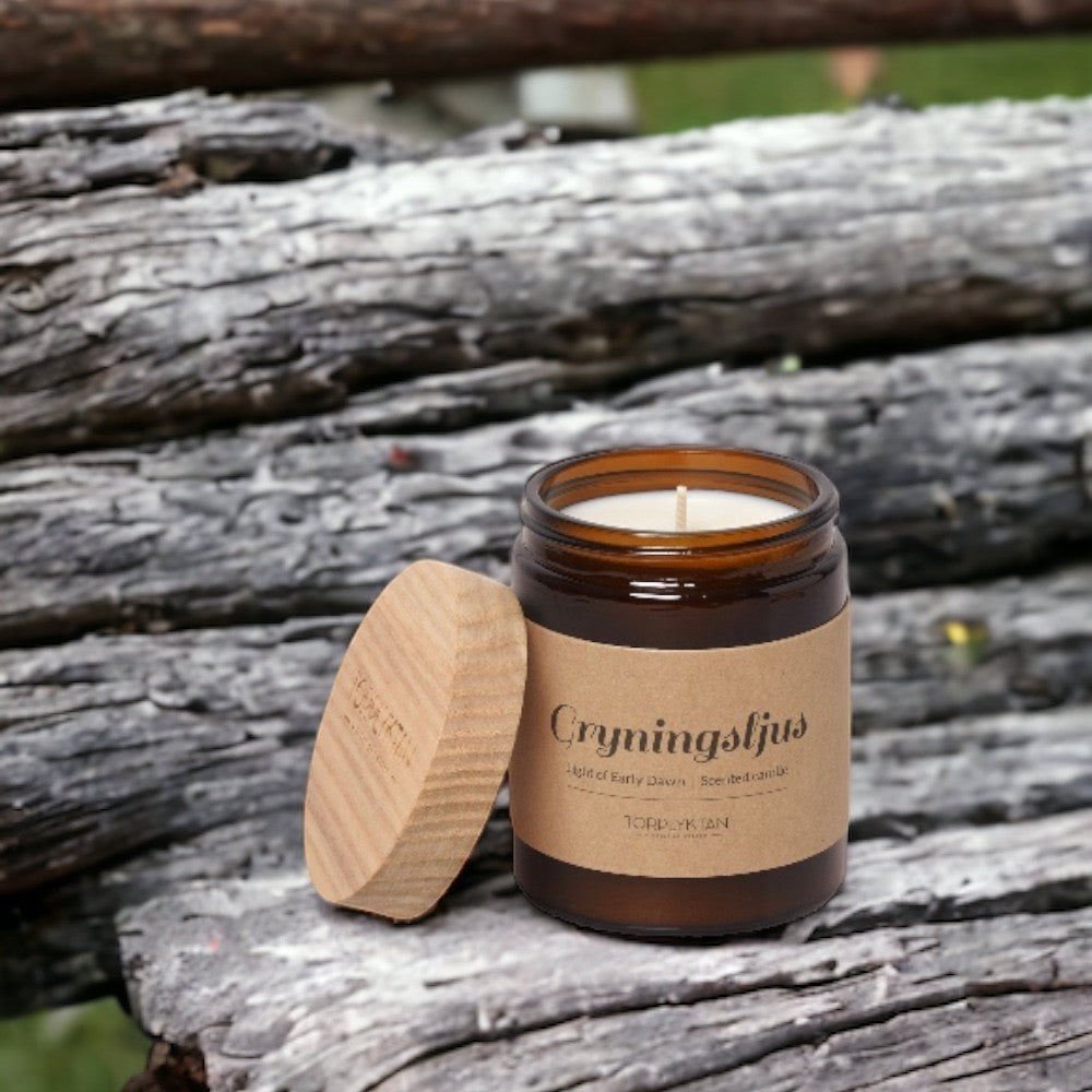 aelgmark amber glass candle with wooden lid, featuring 'Cryningstjlus' and 'Light of Early Dawn' scent notes.