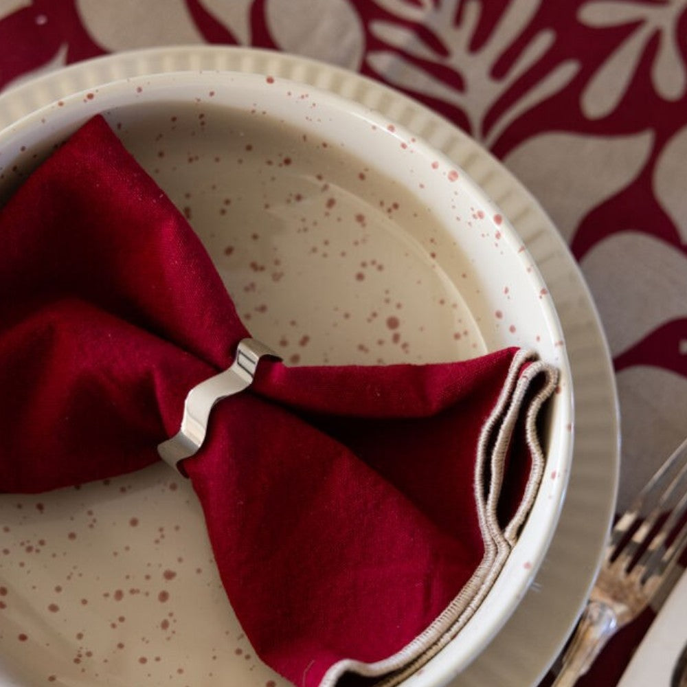 aelgmark Anna silver wave napkin ring holding a red cloth napkin on a speckled plate.