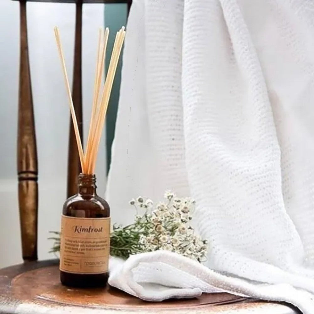 aelgmark Autumn Frost reed diffuser with amber glass bottle, natural reeds, and a white towel. Notes of cedar, iris, vanilla, sandalwood, musk.