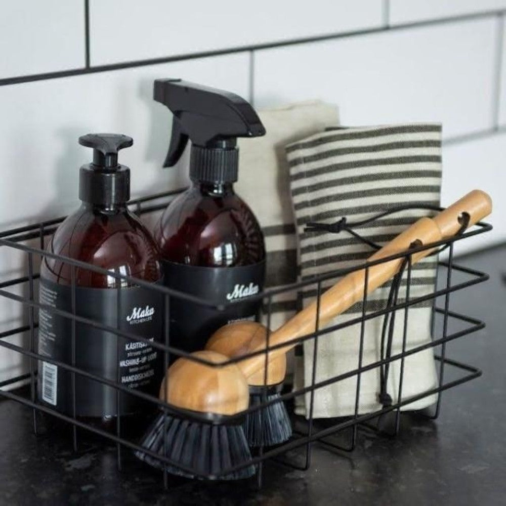 aelgmark bamboo dish brush with wooden handle and black bristles, next to cleaning bottles and striped towel in wire basket.