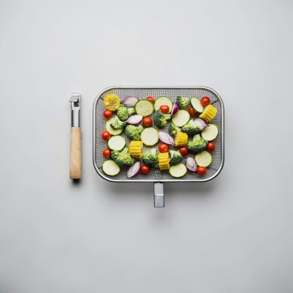 aelgmark Fredde BBQ grill basket with removable wooden handle, filled with chopped vegetables like broccoli, zucchini, corn, tomatoes, and red onion.
