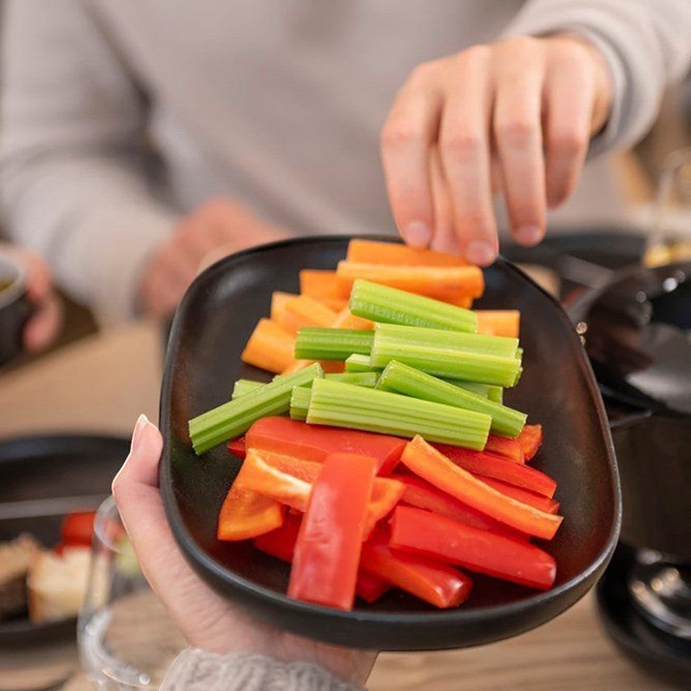 aelgmark black matte oval ceramic serving platter with cut vegetables like carrots, celery, and bell peppers.