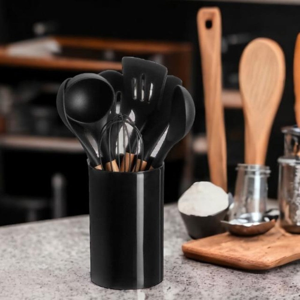 A set of 7 black silicone kitchen utensils with wooden handles, including a whisk, ladle, and spatulas, stored in a black holder. From aelgmark 北歐生活選物.