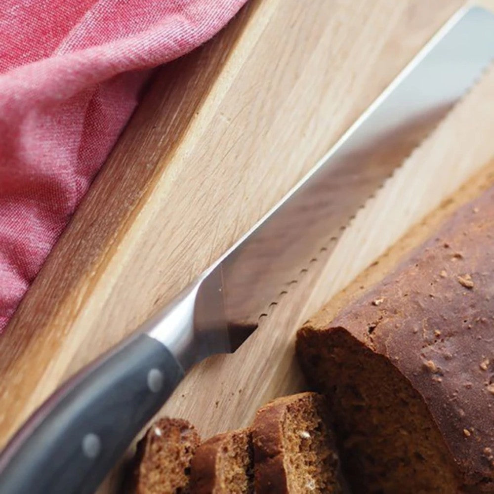 aelgmark bread knife with serrated German vanadium steel blade and pakkawood handle slicing brown bread on a wooden cutting board.
