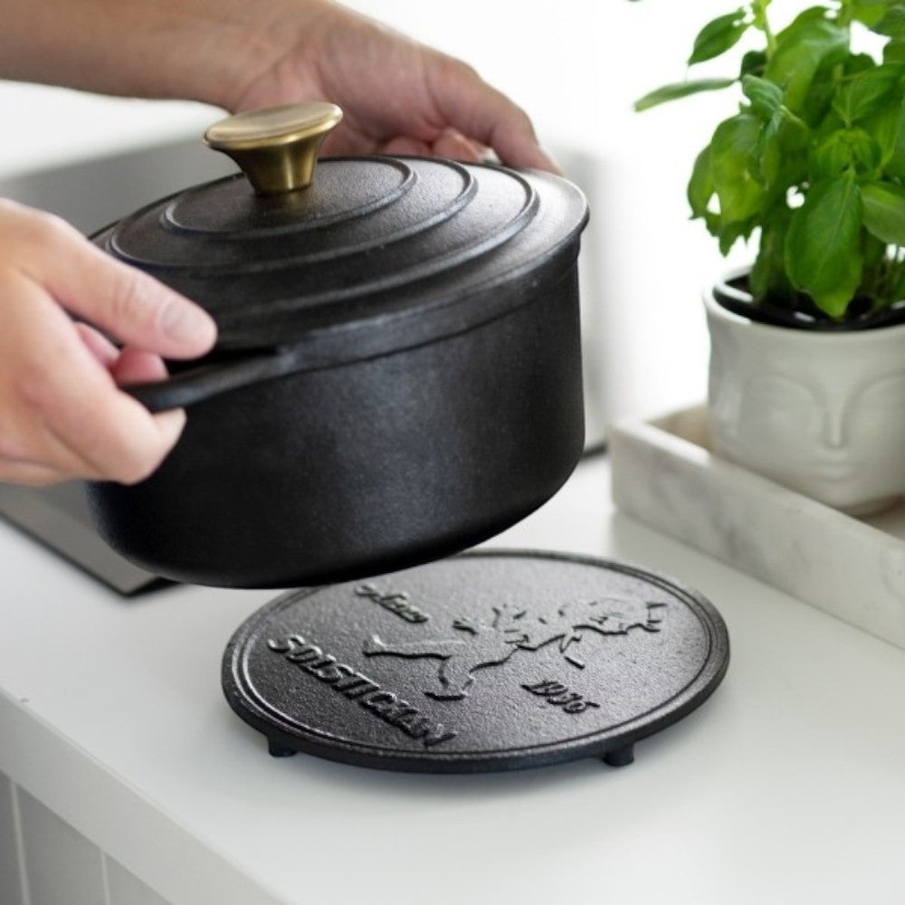 aelgmark cast iron trivet with embossed SOLSTICKAN logo and boy graphic, protecting surfaces from hot pots.