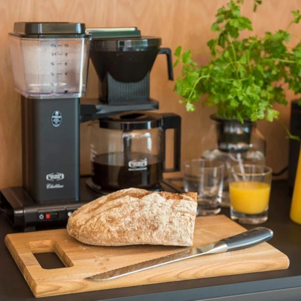 Aelgmark coffee maker with carafe, bread on wooden cutting board, and orange juice.