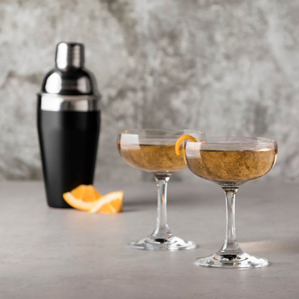 aelgmark two clear glass coupe cocktail glasses with orange garnish and a cocktail shaker.