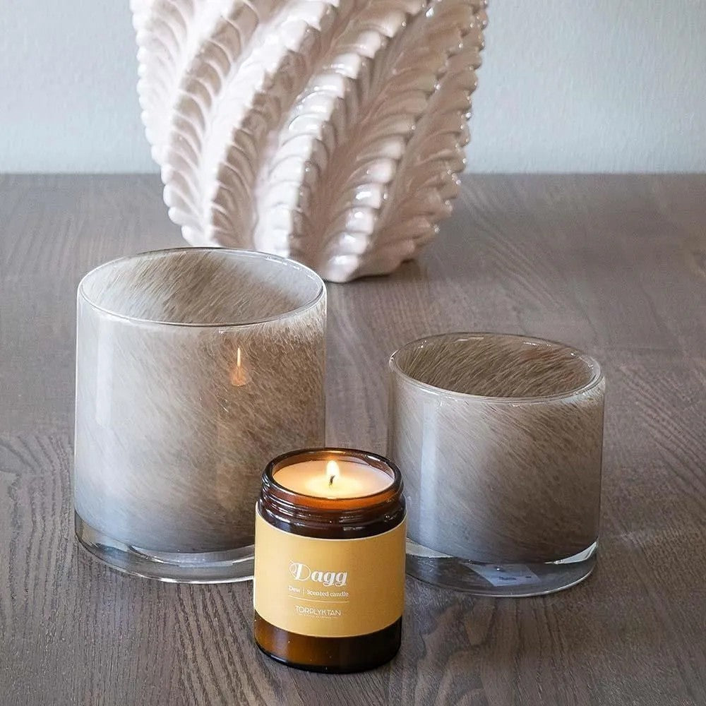 aelgmark Dew scented candle in amber glass jar with yellow label, beside two larger frosted glass candle holders.