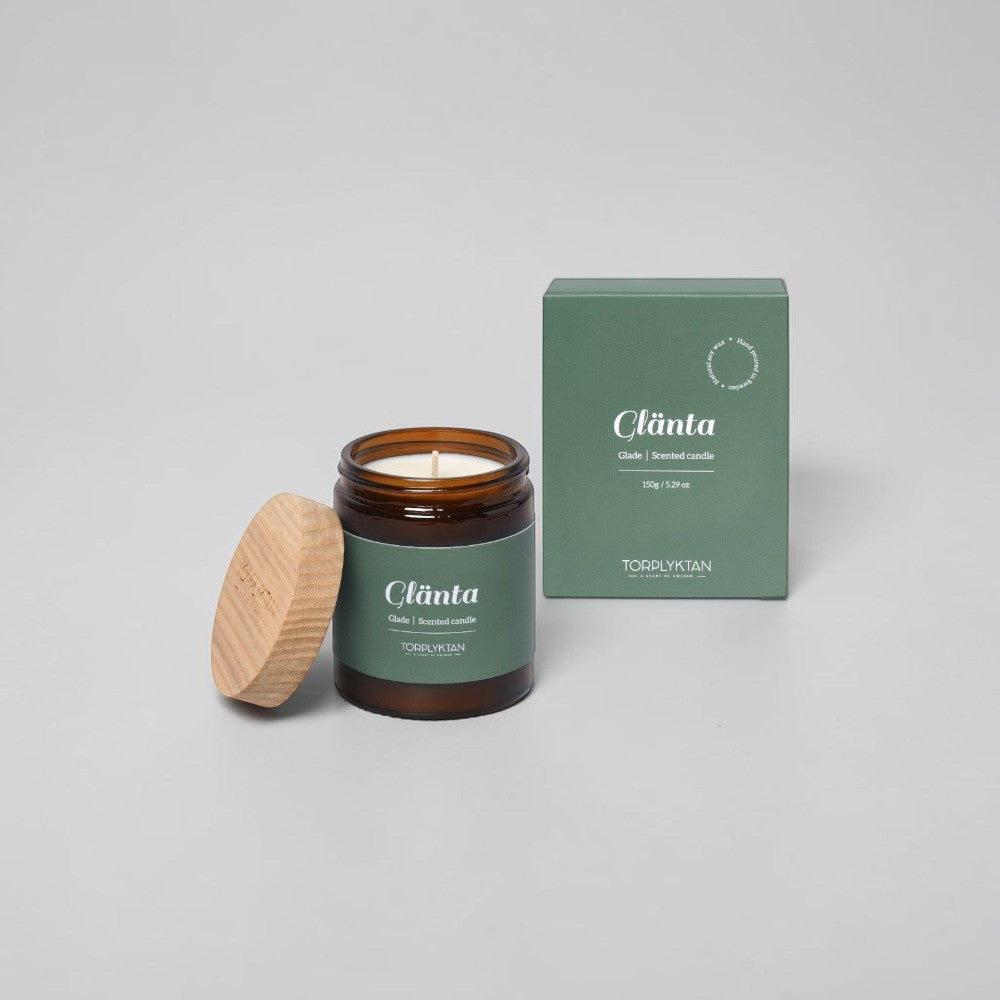 aelgmark Glade scented candle in amber glass jar with wooden lid, 150g, featuring notes of cedar, vetiver, sandalwood, bergamot, apple, and cherry.