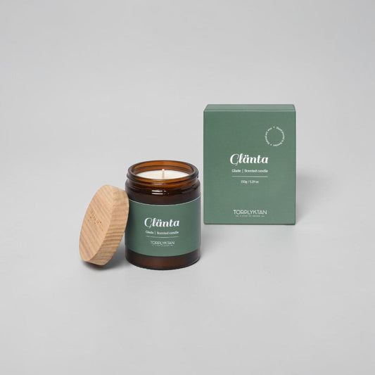 aelgmark Glade scented candle in amber glass jar with wooden lid, 150g, featuring notes of cedar, vetiver, sandalwood, bergamot, apple, and cherry.