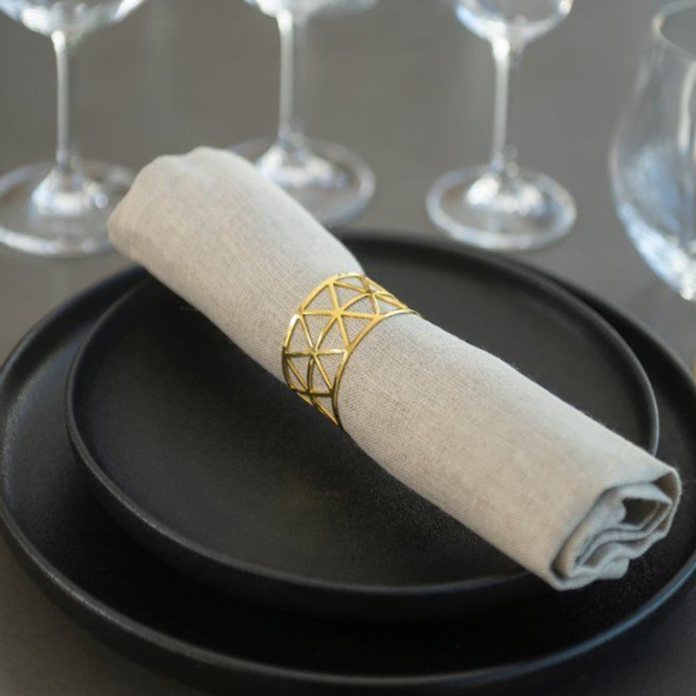 aelgmark gold geometric napkin ring on a linen napkin, set on a black plate.