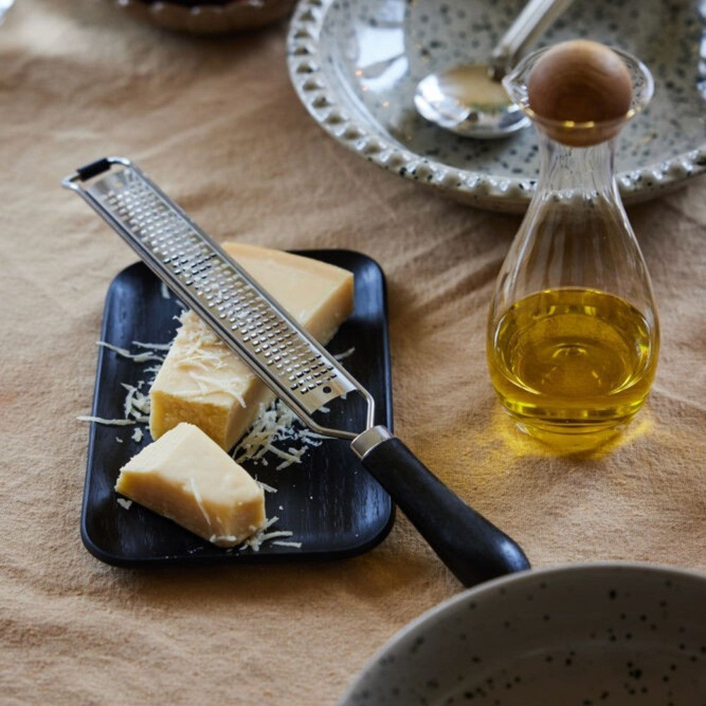 aelgmark北歐生活選物 Hanna matte black rectangular wooden serving dish with rounded edges, holding cheese and a grater.
