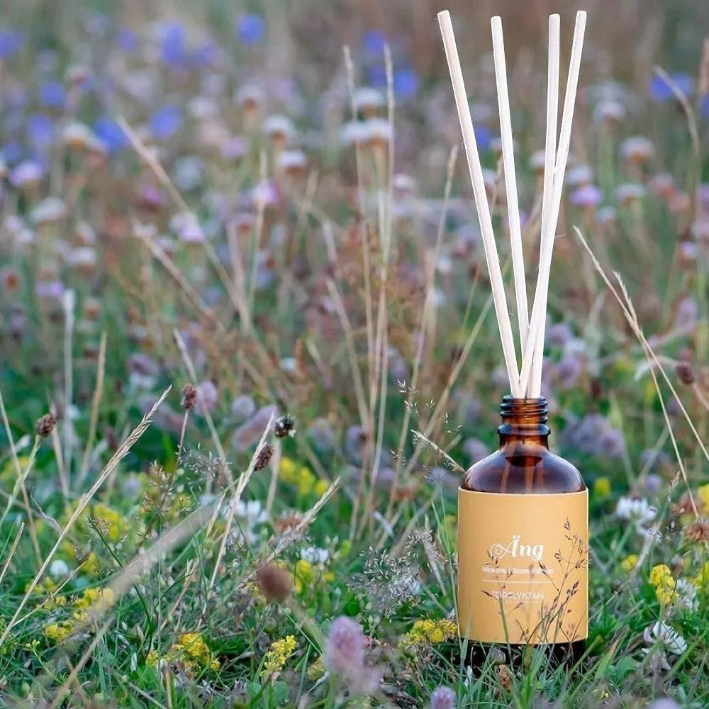 aelgmark Meadow reed diffuser with amber glass bottle and yellow label, set in a field of wildflowers.