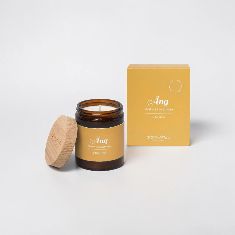 aelgmark Meadow scented candle in amber glass jar with wooden lid, notes of grass, jasmine, sandalwood, and vanilla.