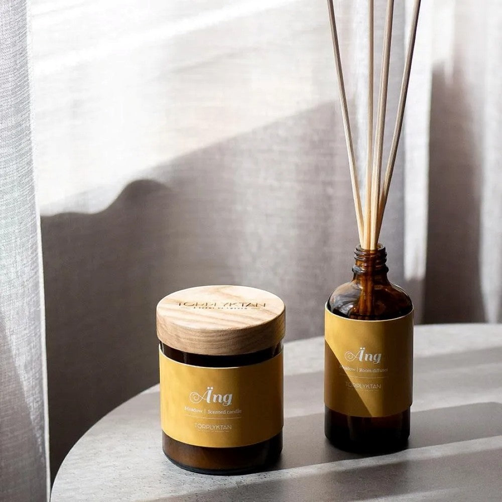 aelgmark Meadow scented candle in amber glass jar with wooden lid and reed diffuser set. Notes of grass, jasmine, sandalwood, and vanilla.