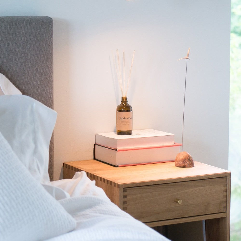 aelgmark diffuser with Midnattssol scent, notes of strawberry, ginger, grapefruit, rose, and vanilla, on a bedside table.