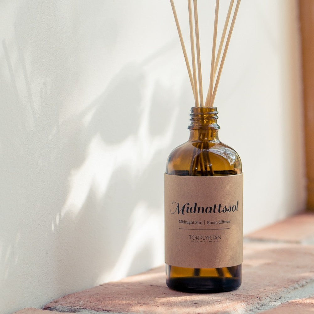 aelgmark amber glass room diffuser with natural reeds, featuring a kraft paper label with 'Midnattsol Midnight Sun' text.
