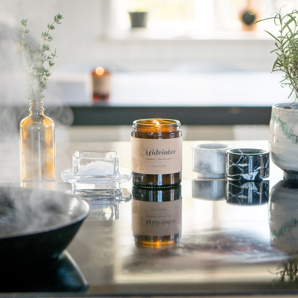 aelgmark Midwinter scented candle in amber glass jar with kraft paper label, featuring notes of sandalwood and vanilla.