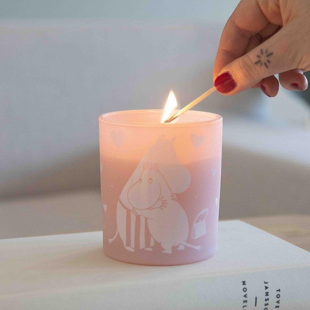 aelgmark Moomin candle in soft pink glass with white Moomin characters hugging and hearts, scented with fresh linen.