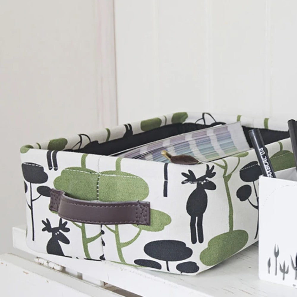 aelgmark storage basket with a Nordic moose and forest pattern in green and black on white fabric, featuring brown leather handles.