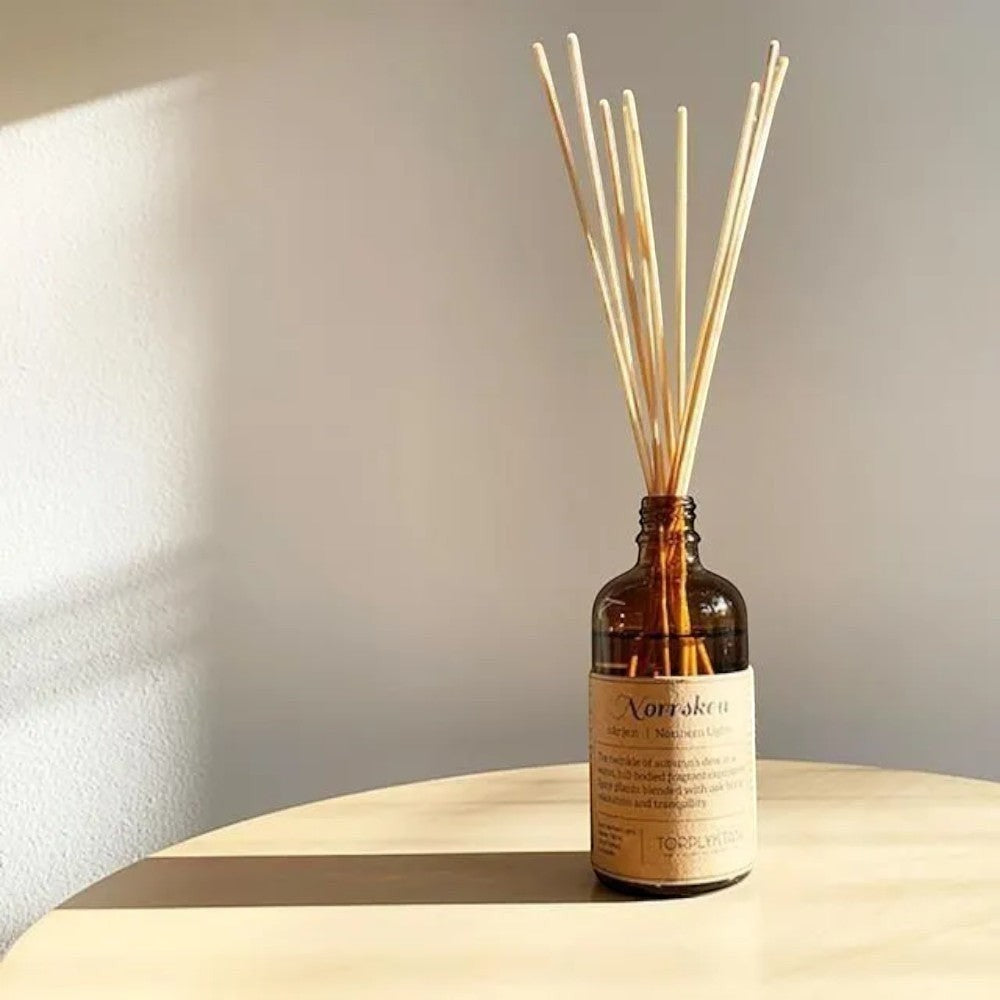 aelgmark Northern Lights reed diffuser in amber glass bottle with natural reeds, warm floral and woody scent.