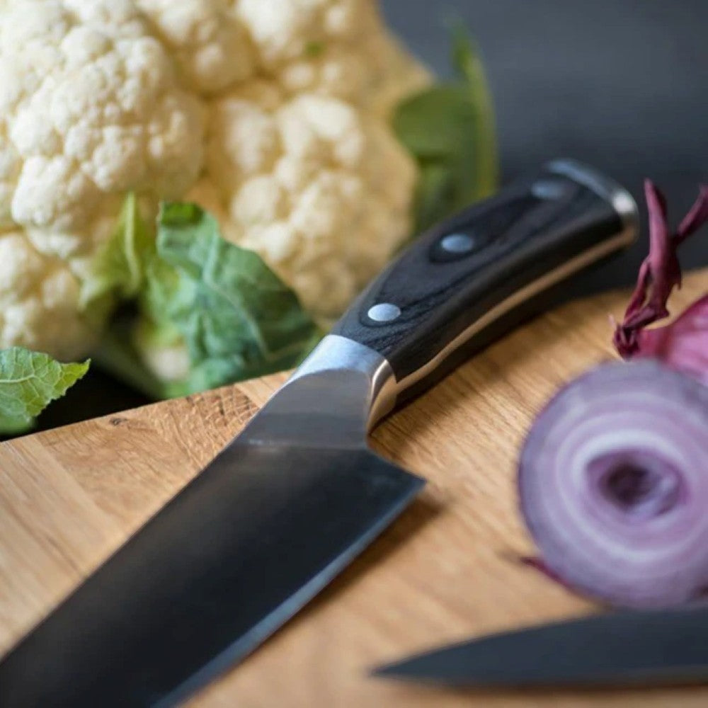 aelgmark chef's knife with black pakkawood handle and German vanadium steel blade, next to cauliflower and red onion.