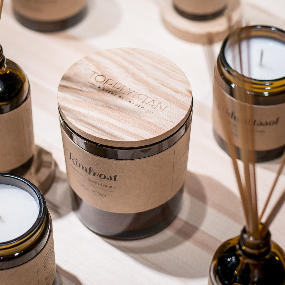 aelgmark Rimfrost scented candle in amber glass jar with wooden lid, featuring notes of cedar, iris, vanilla, sandalwood, and musk.