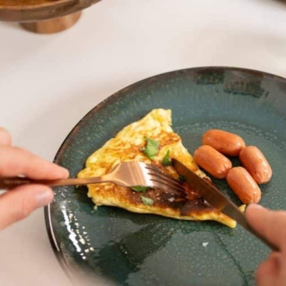Aelgmark rose gold cutlery set, 16-piece stainless steel with PVD coating, used for eating an omelet and sausages.