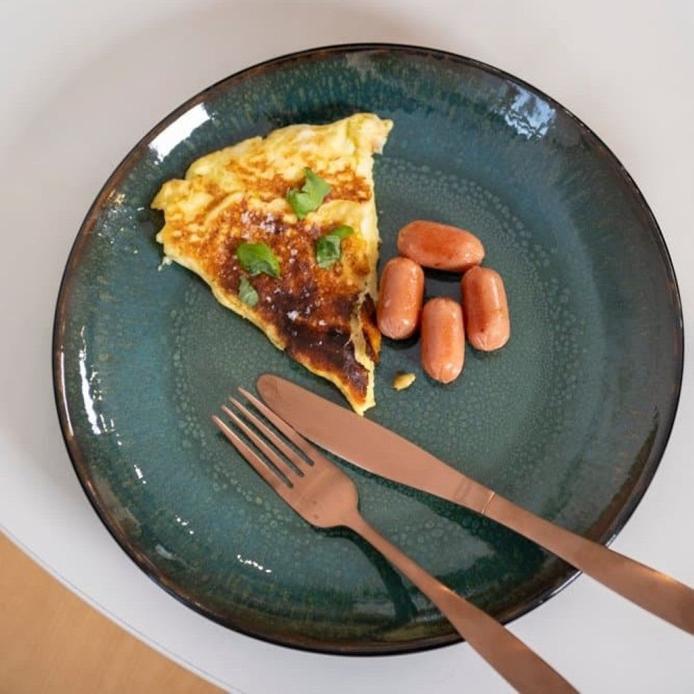 Aelgmark rose gold cutlery set with aelgmark 16-piece stainless steel cutlery set on a teal speckled plate with an omelet and sausages.