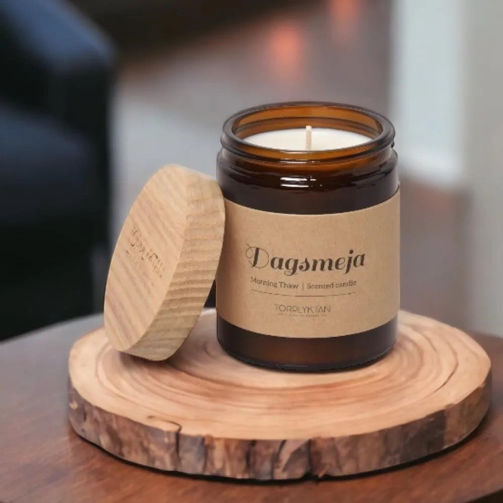 aelgmark scented candle in amber glass jar with wooden lid, featuring a kraft paper label with 'Dagsmeja Morning Thaw' text.