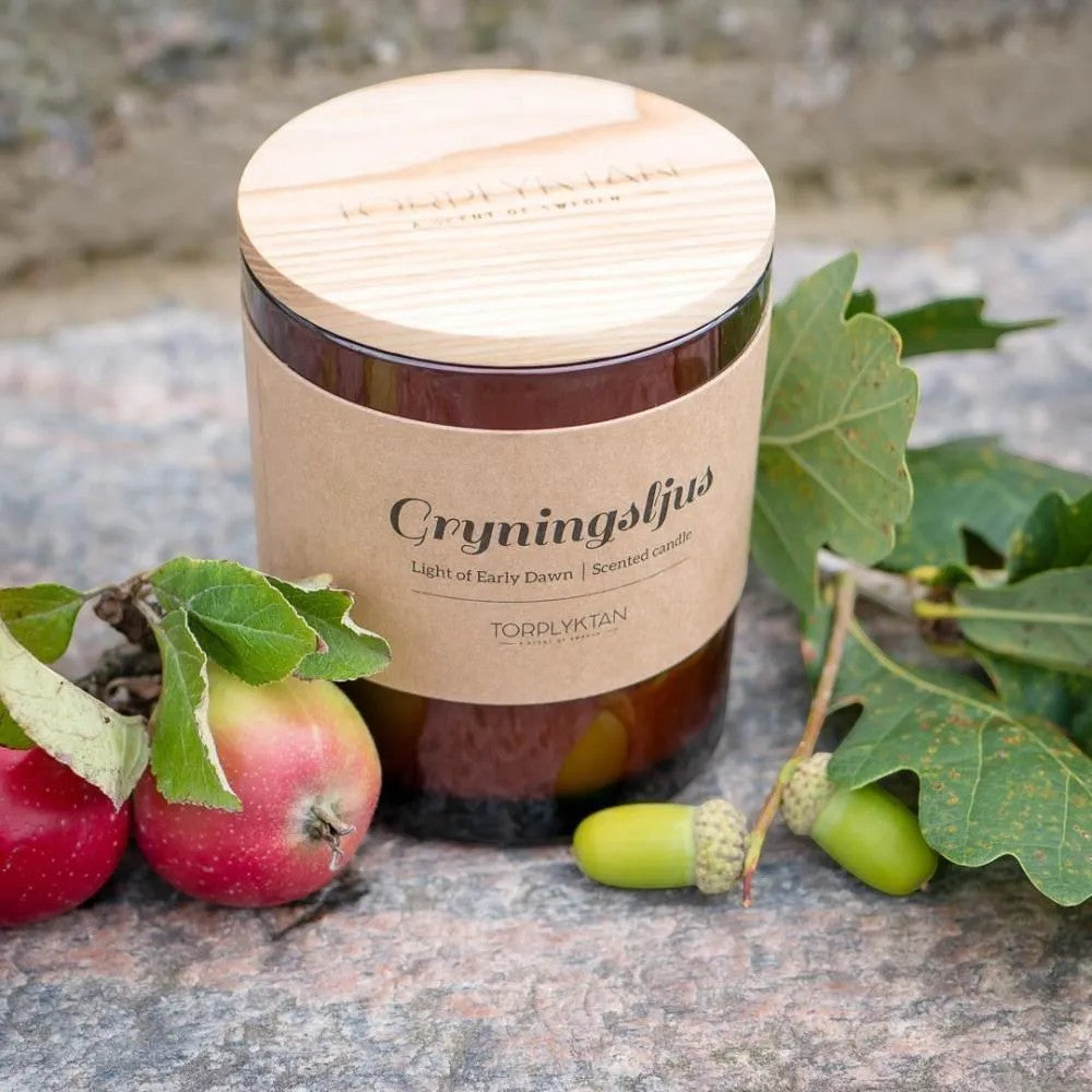 aelgmark scented candle in amber glass jar with wooden lid, featuring notes of oak, apple, and citrus.