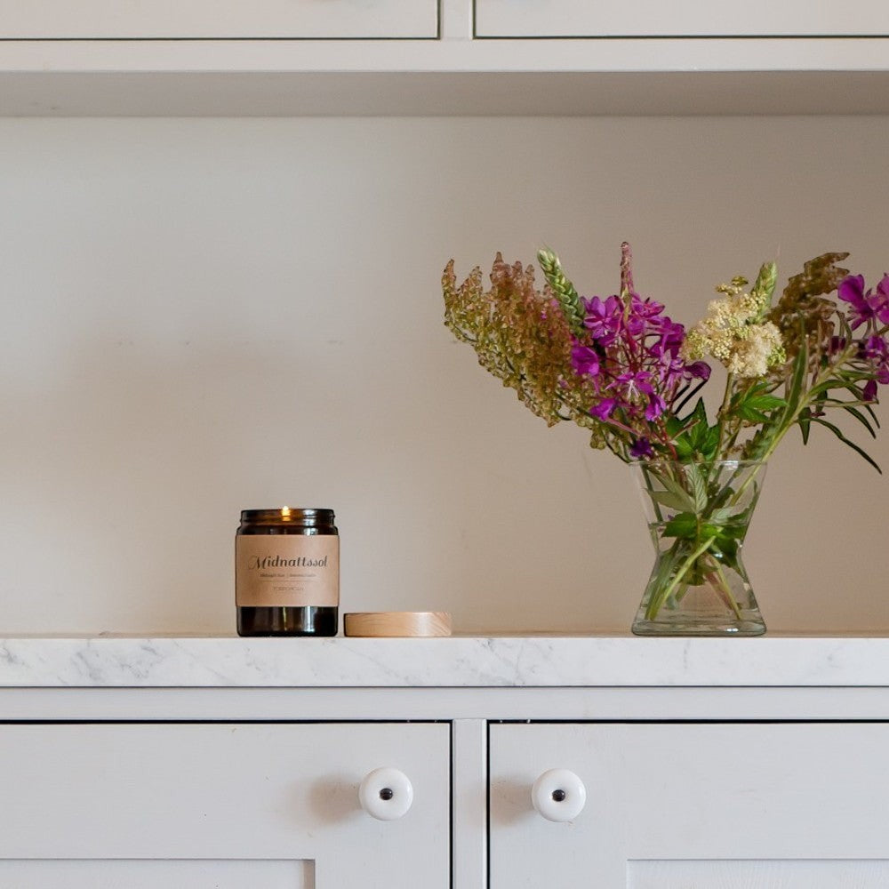aelgmark scented candle in amber glass jar with a light brown label, featuring floral notes of rose and berry.