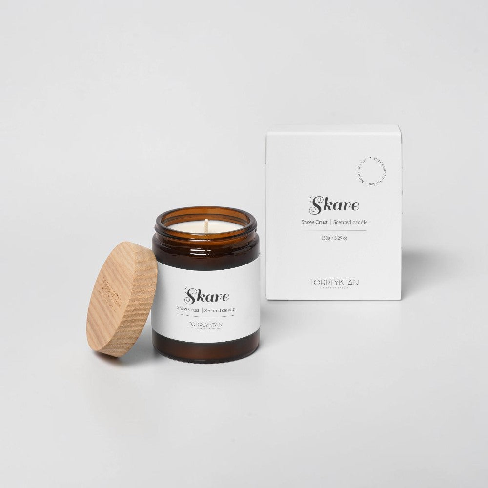 aelgmark Skare Snow Crust scented candle in amber glass jar with wooden lid. Notes of cinnamon, mint, and bergamot.
