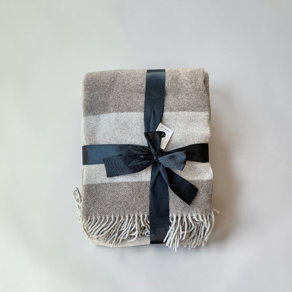 aelgmark Ulle striped merino wool throw blanket in grey and beige with fringed edges, tied with a black ribbon.
