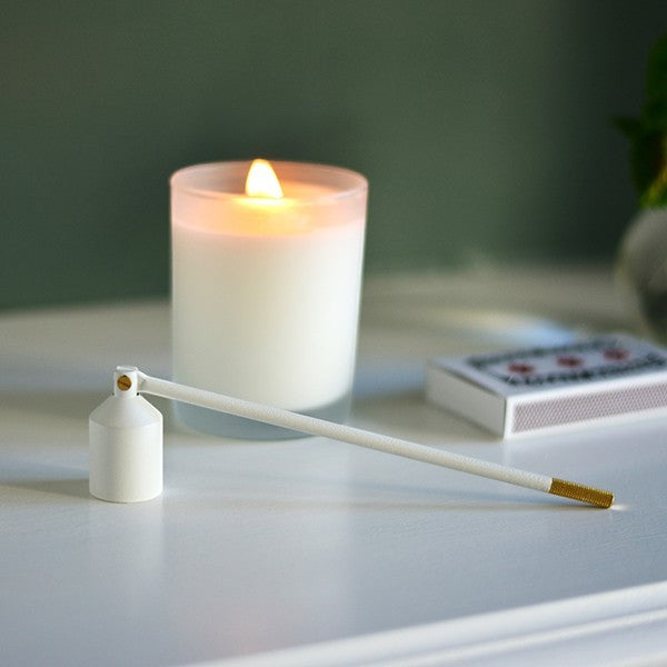 aelgmark white candle snuffer with gold accent, next to a white candle and matches.