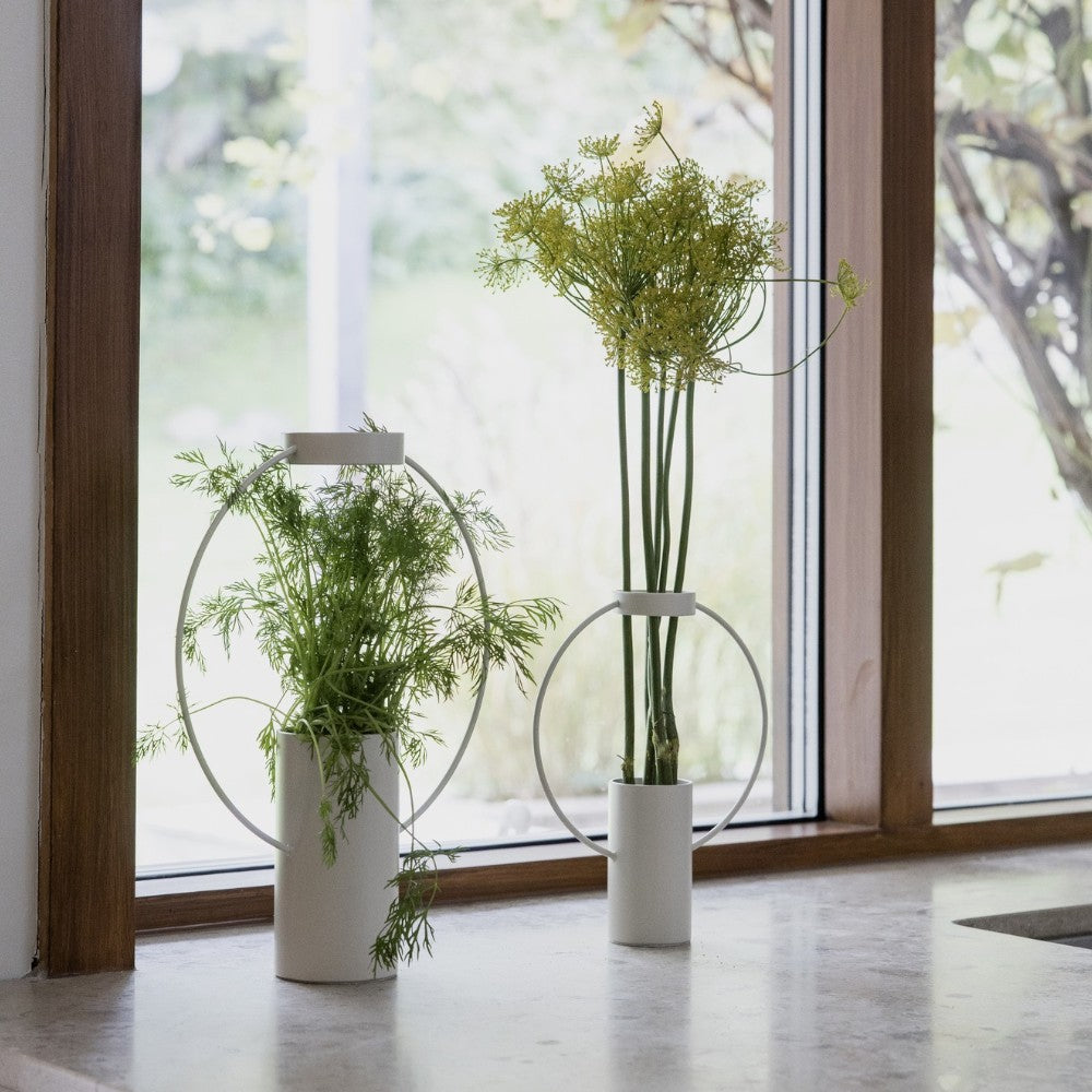 aelgmark modern white iron cylindrical vases with minimalist circular metal frames, holding green plants.