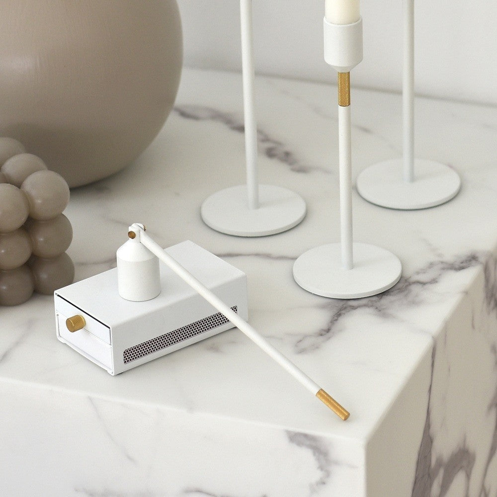 aelgmark white metal match striker box with gold knob and long matchstick with gold tip.