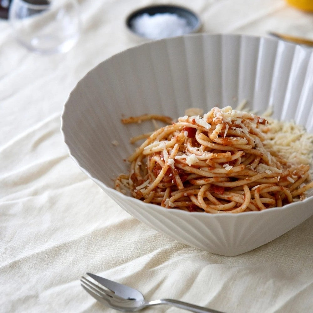 Aelgmark Frances white shell-shaped ceramic bowl filled with spaghetti and topped with grated cheese.