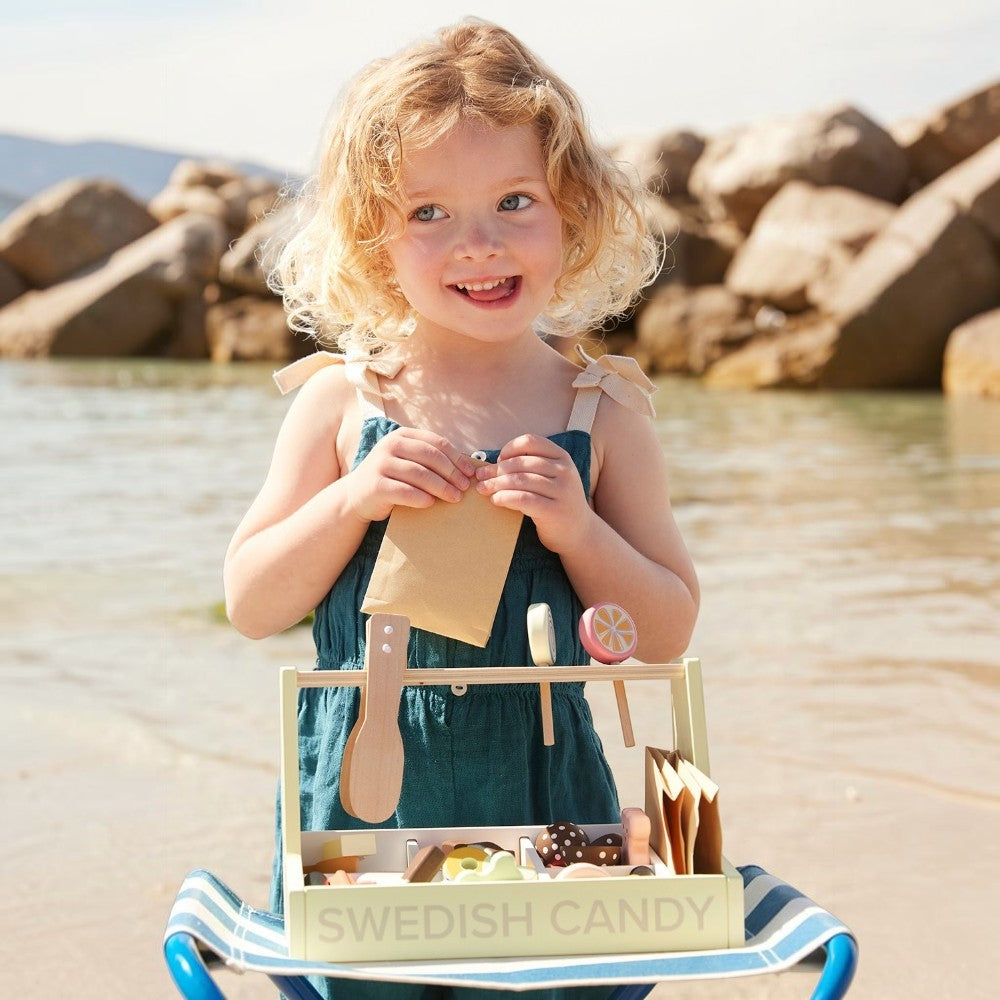 aelgmark

Nordic-style wooden candy shop toy with assorted pretend candies, a scoop, and paper bags. A young girl with blonde curly hair wears a teal dress.